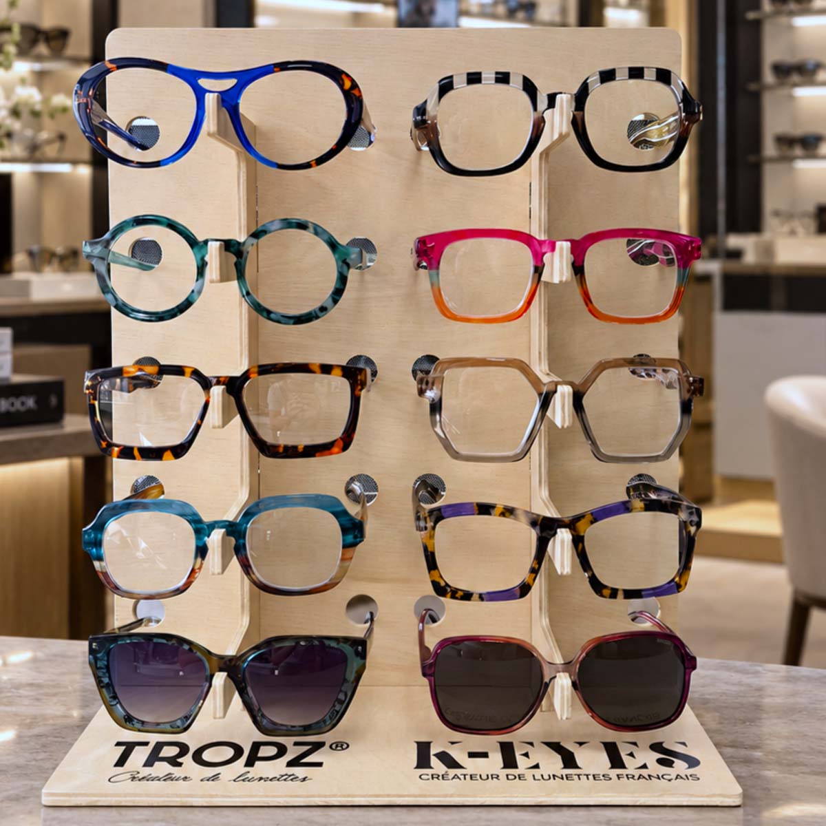 Présentoir en bois TROPZ K-EYES 10 places avec lunettes colorées, idéal pour comptoir de pharmacie et d’opticien.
TROPZ K-EYES wooden 10-place eyewear display with colorful glasses, designed for pharmacy and optician counters.